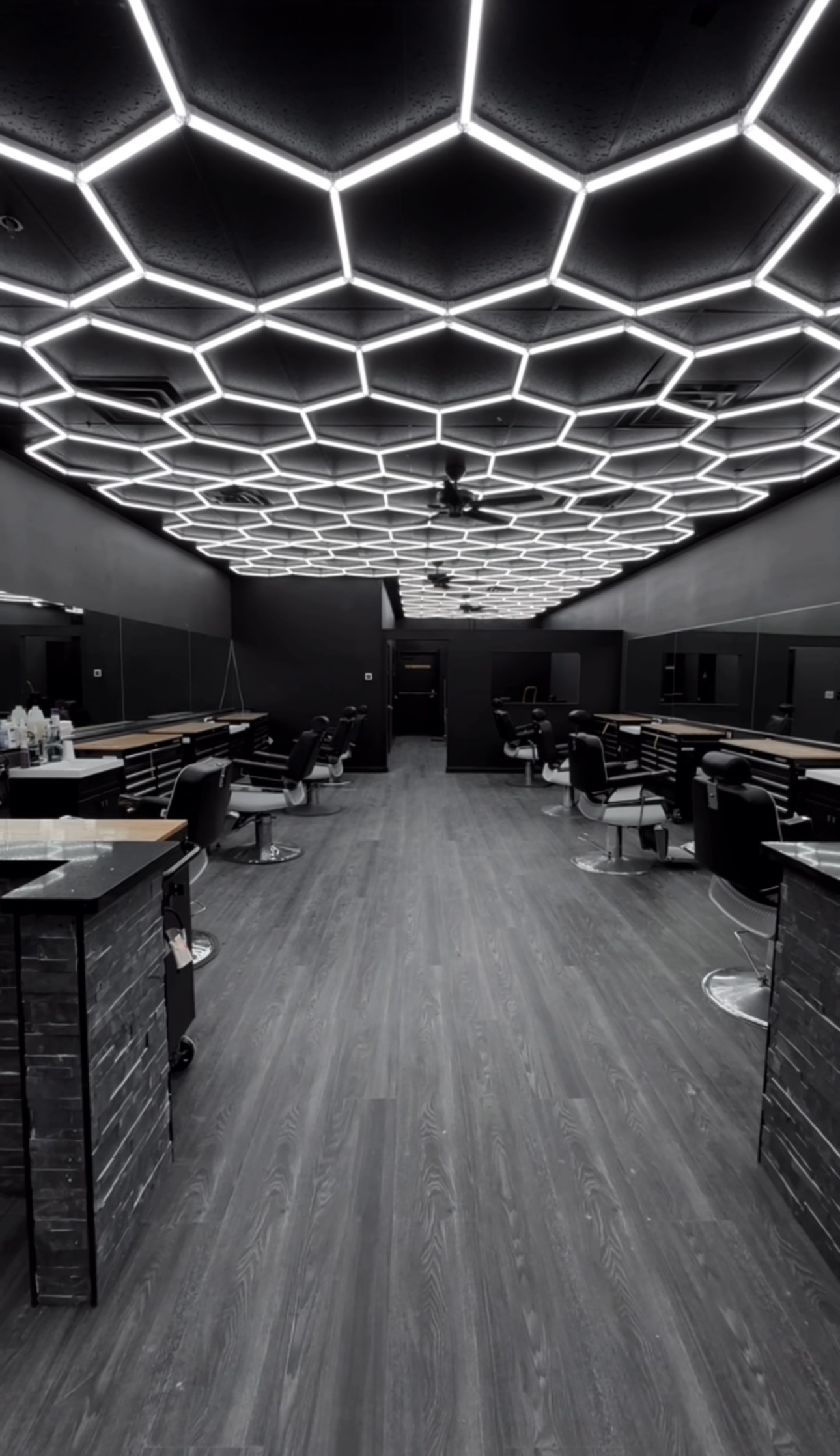 Modern black barbershop interior with hexagon LED ceiling lighting and rows of barber chairs